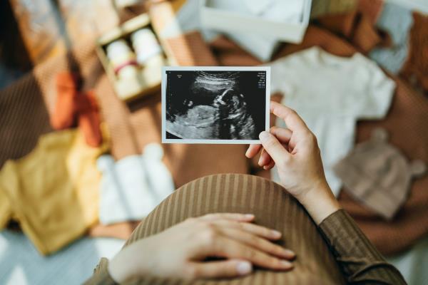 Woman looking at an ultrasound scan photo while gently touching her baby bump